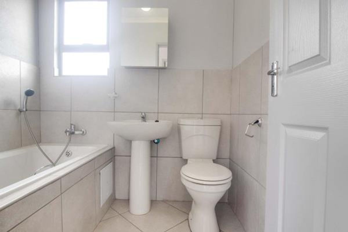 A clean, functional bathroom featuring a pedestal basin, toilet, and bathtub with tiled finishes throughout.