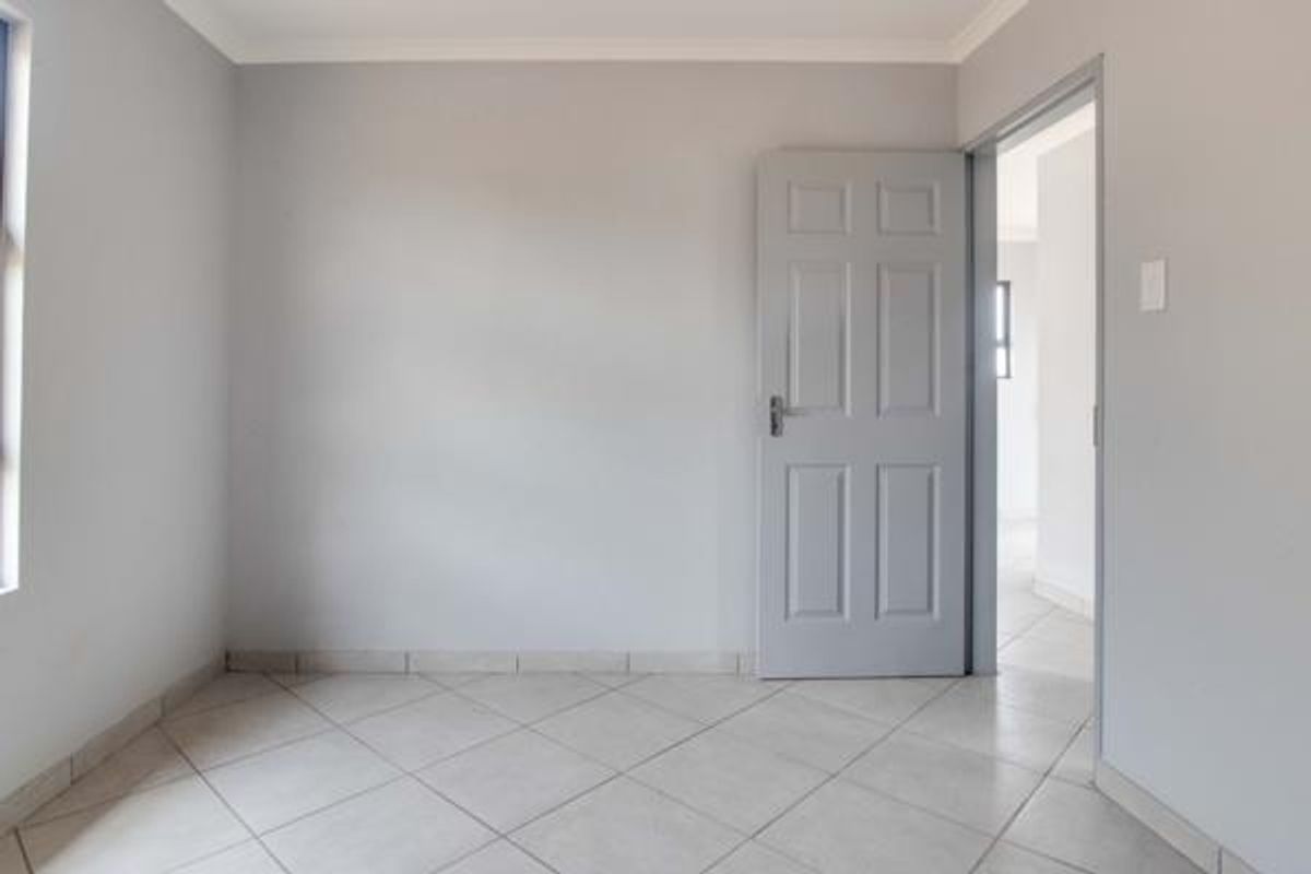 A clean, empty bedroom featuring neutral grey walls, tiled flooring, and a classic six-panel interior door, offering a blank canvas for personalization.