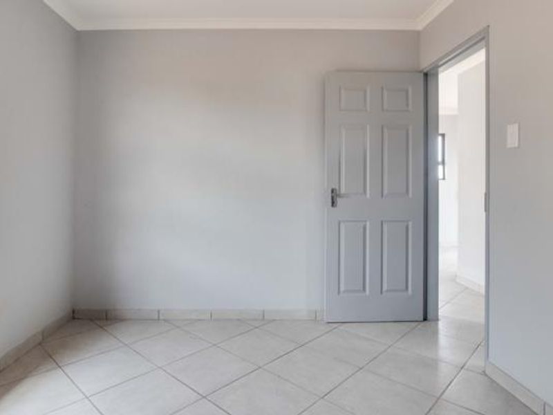 A clean, empty bedroom featuring neutral grey walls, tiled flooring, and a classic six-panel interior door, offering a blank canvas for personalization.