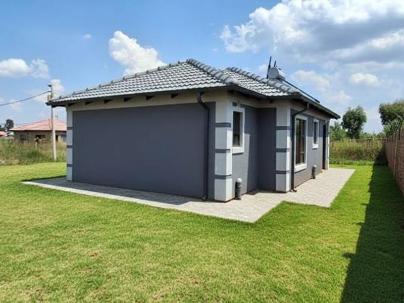 Rear view of the house featuring a tiled roof, solar geyser, paved perimeter walkway, and secure electric fencing surrounding the property.