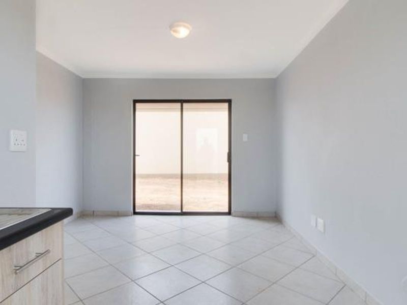 An empty open-plan living area featuring neutral wall paint, ceramic floor tiles, and a sliding glass door providing access to the exterior.