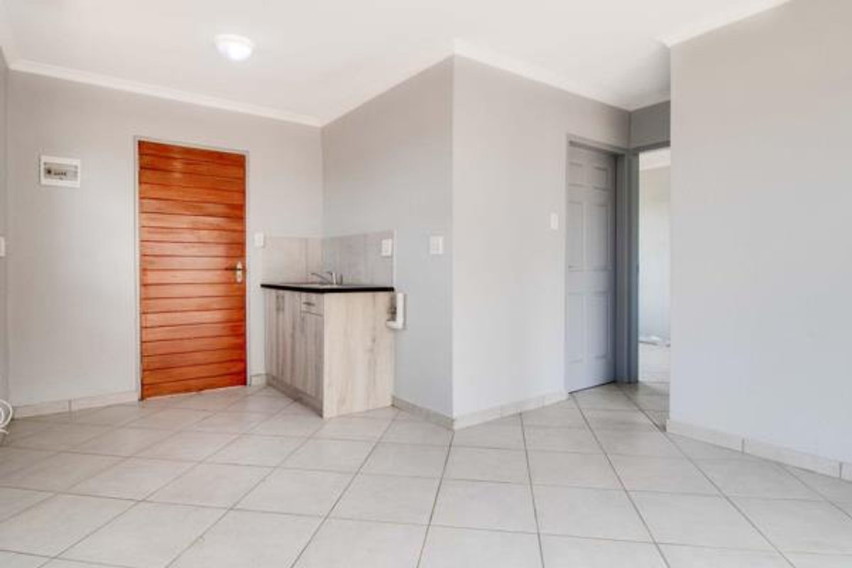 A clean, empty scullery or utility area featuring tiled flooring, built-in cabinetry with a sink, and neutral wall finishes.