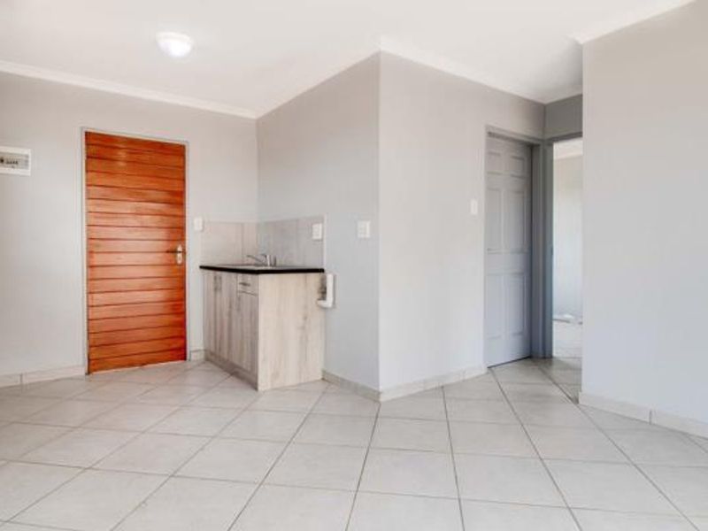 A clean, empty scullery or utility area featuring tiled flooring, built-in cabinetry with a sink, and neutral wall finishes.