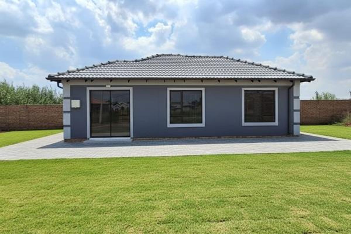 Rear view of a modern single-story house featuring a tiled roof, grey exterior walls, sliding glass doors, and a well-maintained lawn with paved patio.