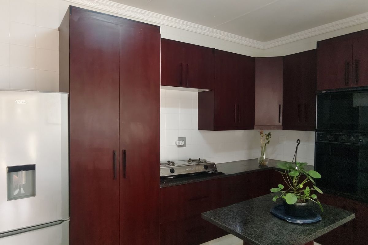 A functional kitchen featuring dark wood cabinetry, granite countertops, a built-in oven, and a gas hob with a tiled backsplash.