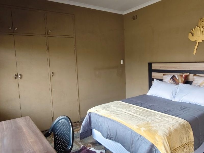 A bedroom featuring built-in cupboards, tiled flooring, and venetian blinds, offering a functional space with potential for cosmetic updates.