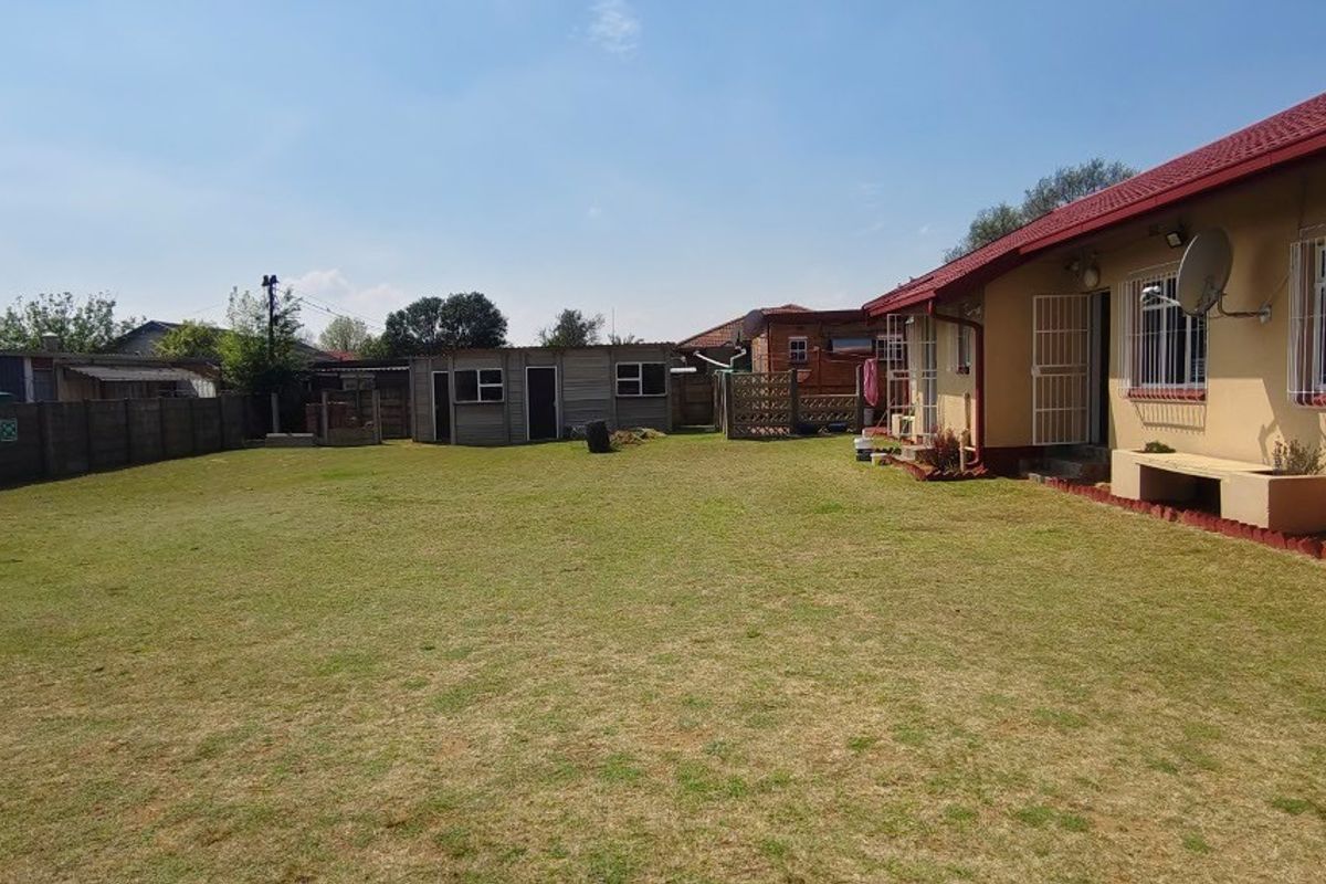 Spacious rear garden featuring a large lawn, concrete boundary wall, and an outbuilding, with the main house structure showing standard exterior finishes.