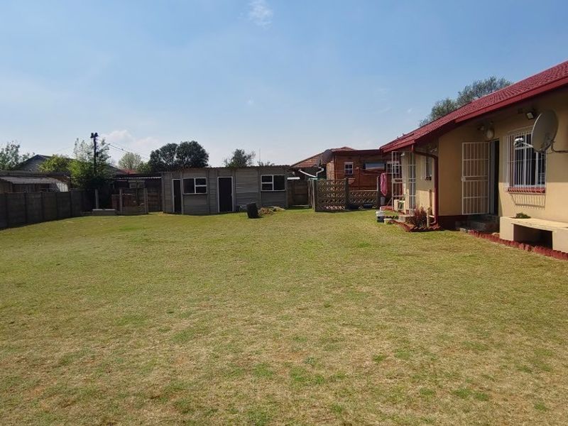 Spacious rear garden featuring a large lawn, concrete boundary wall, and an outbuilding, with the main house structure showing standard exterior finishes.