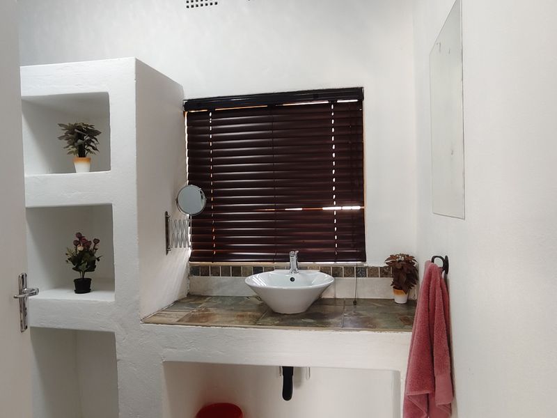A functional bathroom featuring a vessel sink set into a tiled vanity countertop, complemented by built-in shelving and dark venetian blinds.