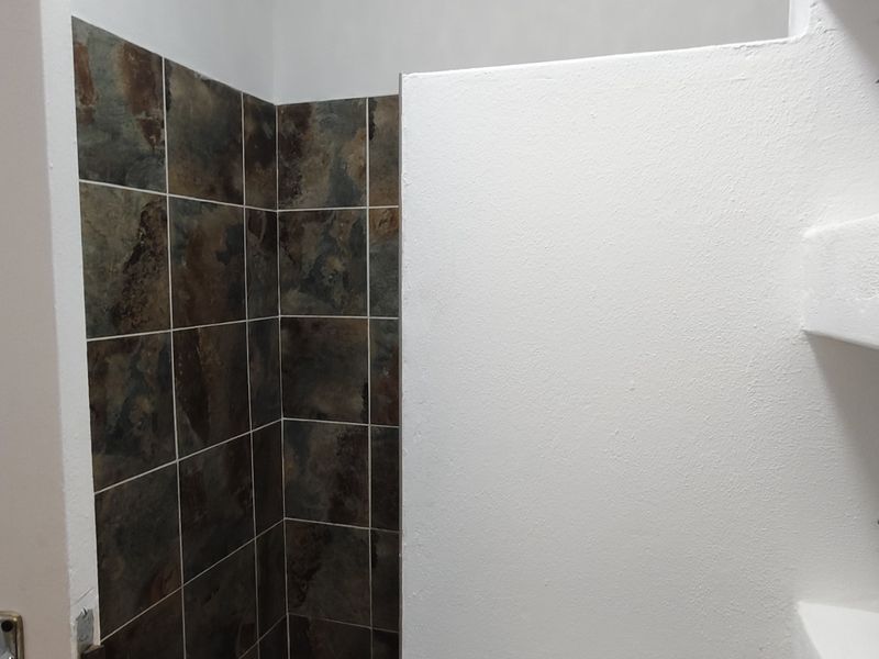 A bathroom shower area featuring dark textured wall tiles and built-in white plastered shelving units.