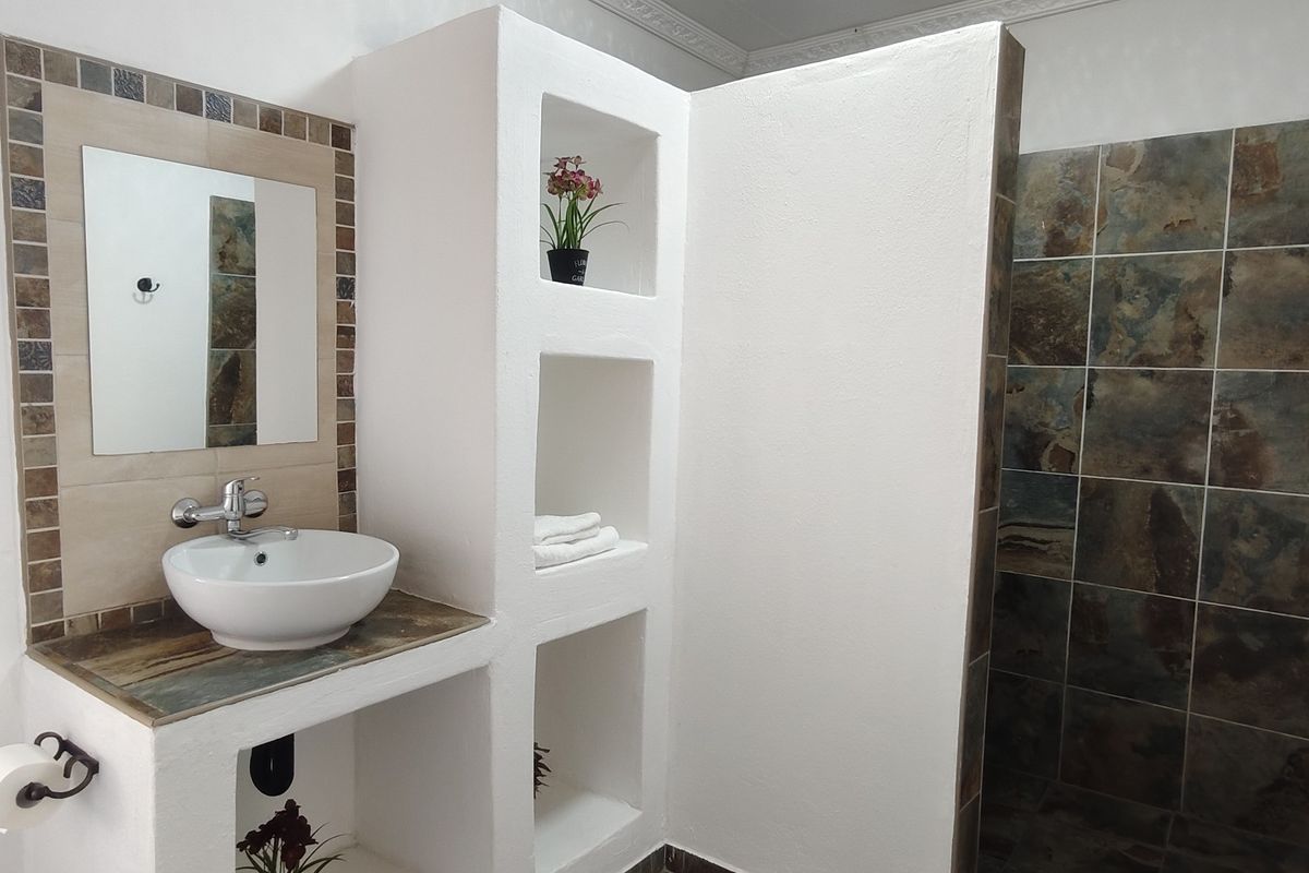 A well-maintained bathroom featuring a modern vessel sink, built-in vanity with integrated shelving, and a tiled shower enclosure with decorative accents.