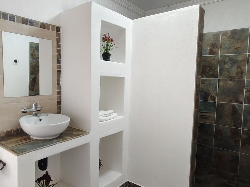 A well-maintained bathroom featuring a modern vessel sink, built-in vanity with integrated shelving, and a tiled shower enclosure with decorative accents.