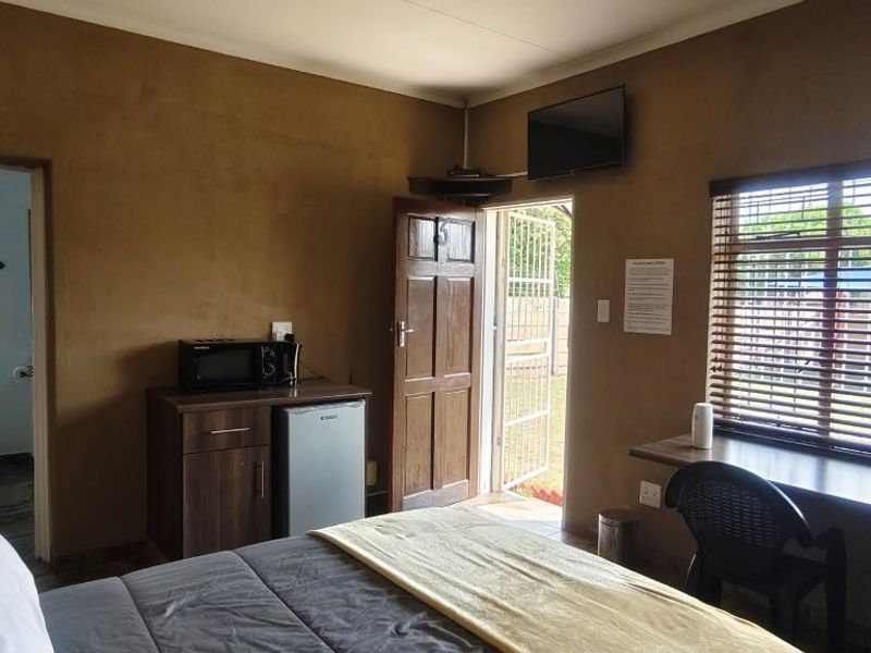 A functional bedroom featuring a built-in desk, venetian blinds, and direct access to an en-suite bathroom, with a security gate leading to the exterior.