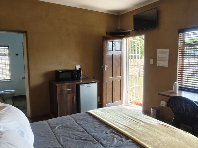 A guest bedroom featuring a built-in desk, timber door with security gate, and venetian blinds, with an adjoining en-suite bathroom.