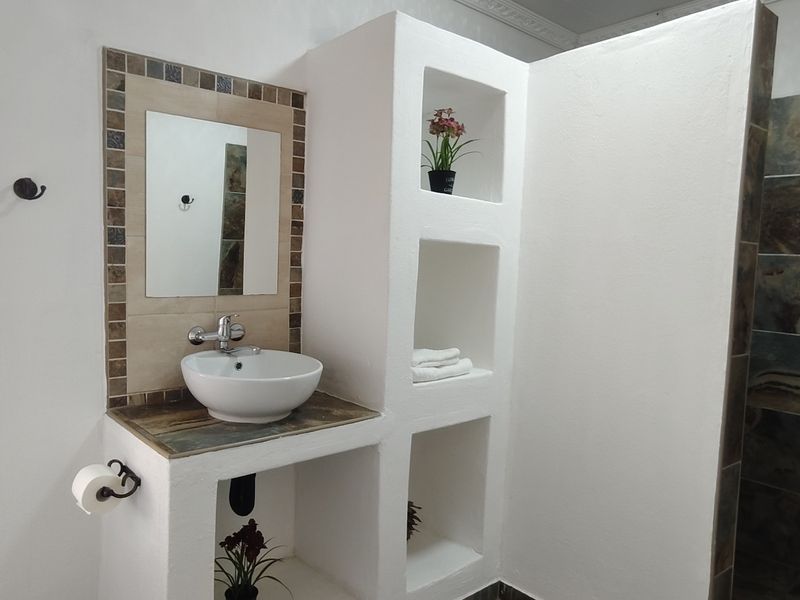 A clean bathroom featuring a vessel sink on a built-in vanity, integrated wall shelving, and a tiled shower enclosure.
