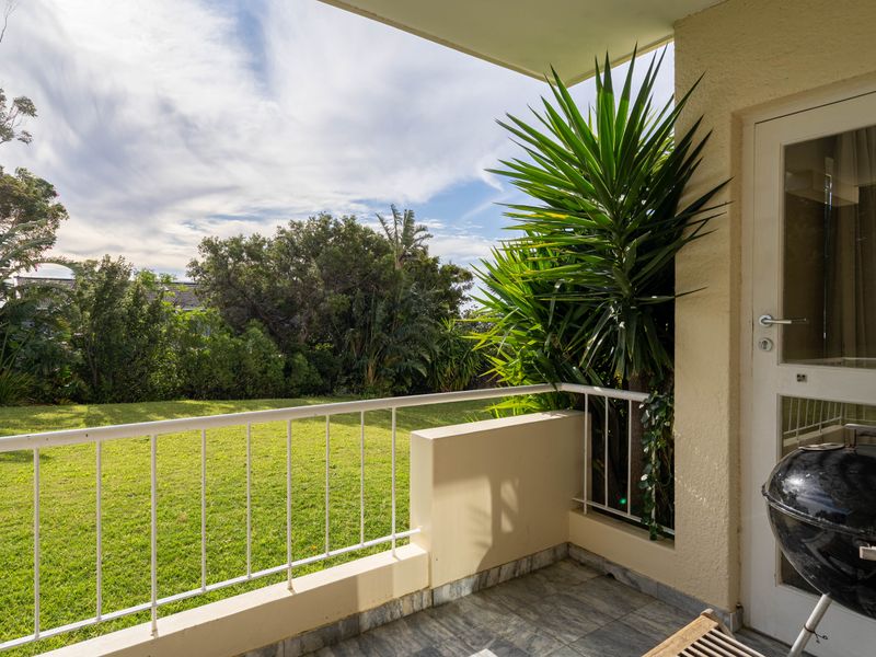 A covered balcony featuring tiled flooring and a metal balustrade, offering direct access to a lush green garden area.