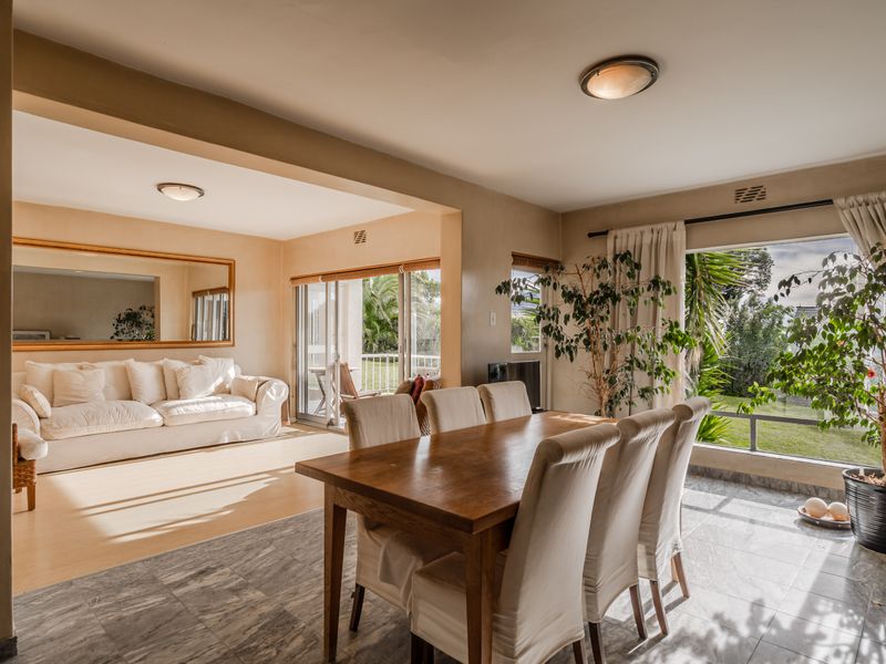 Spacious open-plan living and dining area featuring tiled and laminate flooring, large windows, and sliding glass doors leading to an outdoor space.