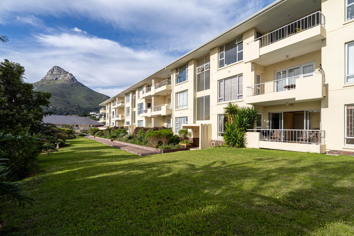 Rear view of the apartment complex featuring private balconies, sliding glass doors, and a well-maintained communal garden with mountain views.