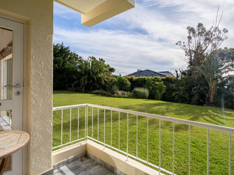 A covered balcony featuring a metal balustrade and tiled flooring, overlooking a well-maintained private garden area.