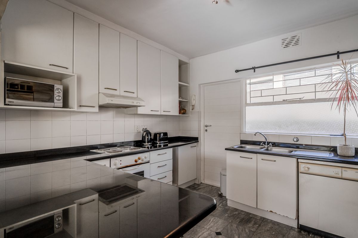 Functional kitchen featuring white cabinetry, black granite countertops, built-in oven, electric hob, and a double sink with tiled backsplash.