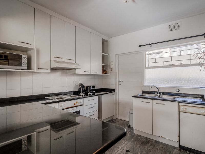 Functional kitchen featuring white cabinetry, black granite countertops, built-in oven, electric hob, and a double sink with tiled backsplash.