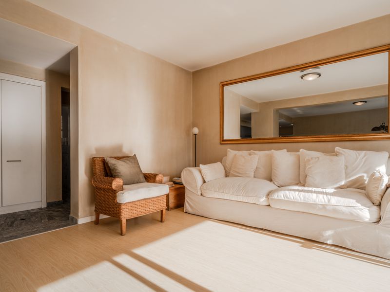 A bright and inviting living room featuring light laminate flooring, neutral wall tones, and a large wall-mounted mirror, creating a spacious and airy atmosphere.