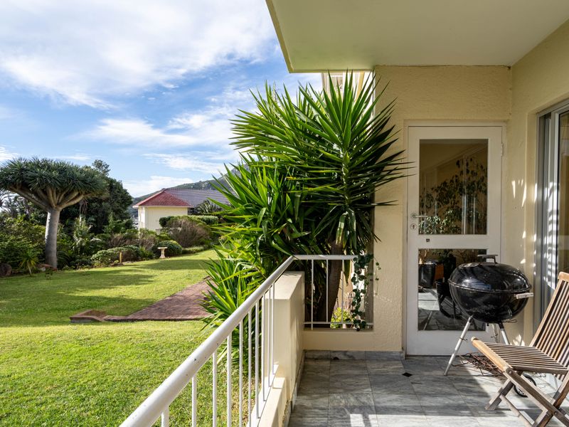 A covered balcony featuring tiled flooring and a metal balustrade, offering direct access to the garden area through a glass door.