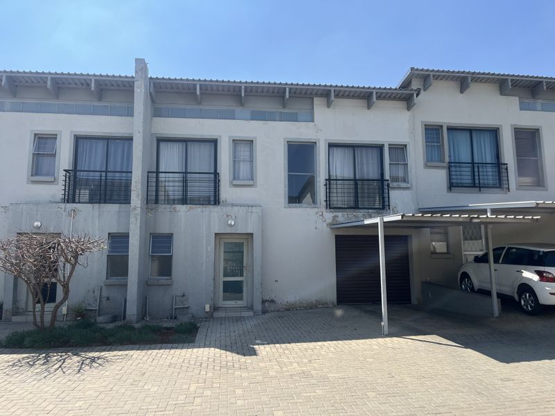 Front elevation of a townhouse complex featuring a paved driveway, carport, garage, and upper-level balconies with metal railings.