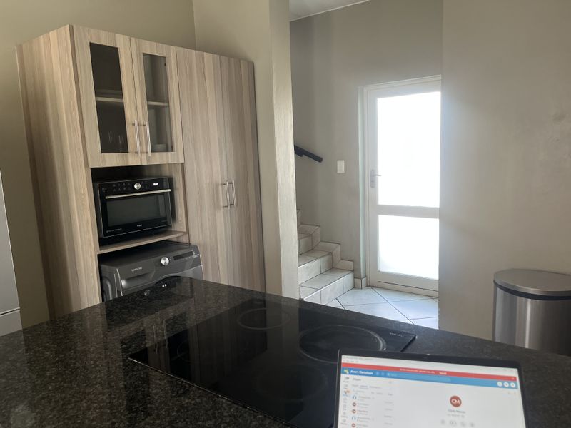 Modern kitchen featuring granite countertops, integrated cooktop, and built-in cabinetry, with an adjacent staircase leading to an exterior door.