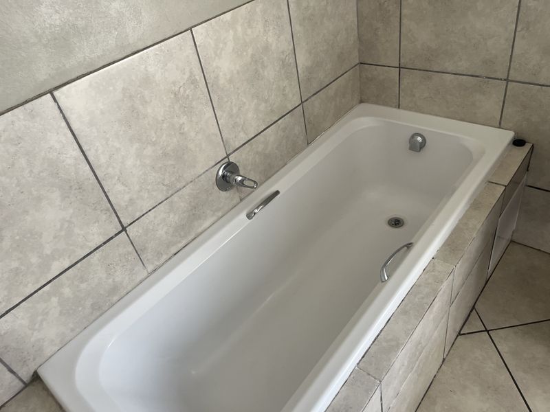 A clean bathroom featuring a built-in bathtub with wall-mounted fixtures and neutral ceramic tiling throughout.