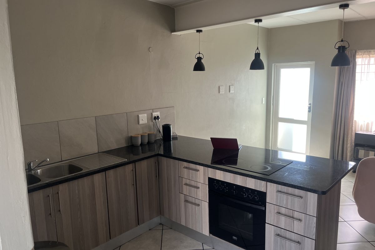 Modern kitchen featuring wood-grain cabinetry, granite countertops, built-in oven, electric hob, and stylish pendant lighting, offering a functional and contemporary cooking space.