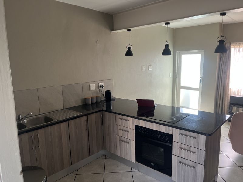 Modern kitchen featuring wood-grain cabinetry, granite countertops, built-in oven, electric hob, and stylish pendant lighting, offering a functional and contemporary cooking space.