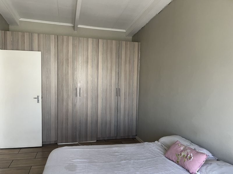 A bedroom featuring built-in cupboards with a wood-grain finish, tiled flooring, and exposed ceiling beams.