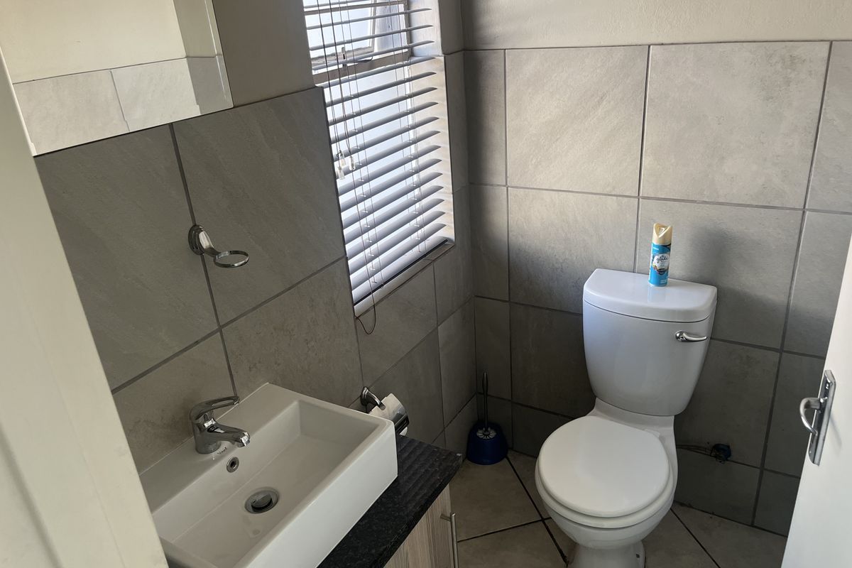 A compact bathroom featuring modern grey wall tiles, a vessel sink vanity, and a standard toilet with venetian blinds for privacy.
