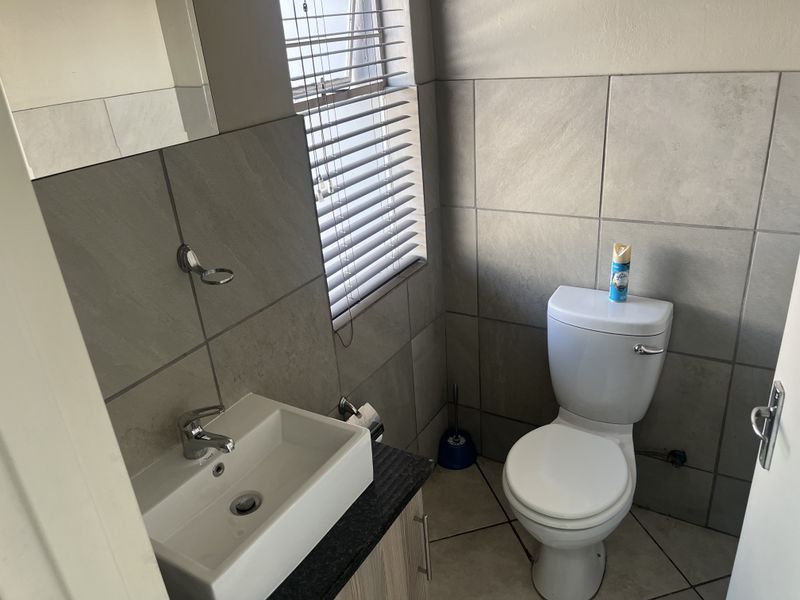 A compact bathroom featuring modern grey wall tiles, a vessel sink vanity, and a standard toilet with venetian blinds for privacy.