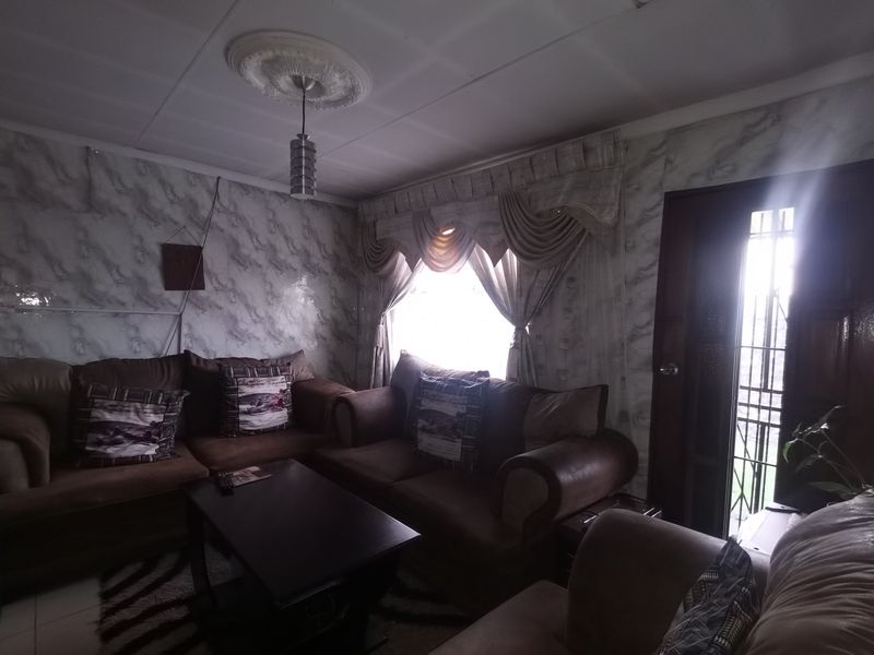 A living room featuring a ceiling rose and security gate access, currently requiring cosmetic updates to modernize the wall finishes and overall aesthetic.