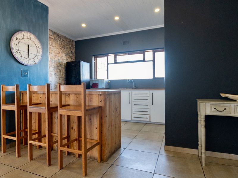 A modern kitchen featuring a wooden breakfast island, white cabinetry, tiled flooring, and a feature wall with stone cladding and blue paint.