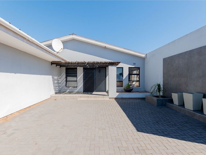 A well-maintained front entrance area featuring a paved driveway, a timber pergola over the doorway, and a modern tiled feature wall.