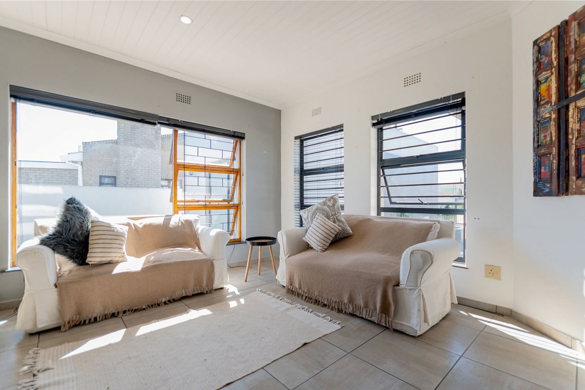 Bright living room featuring tiled flooring, large aluminium windows with security bars, and a clean, neutral aesthetic with recessed ceiling lighting.