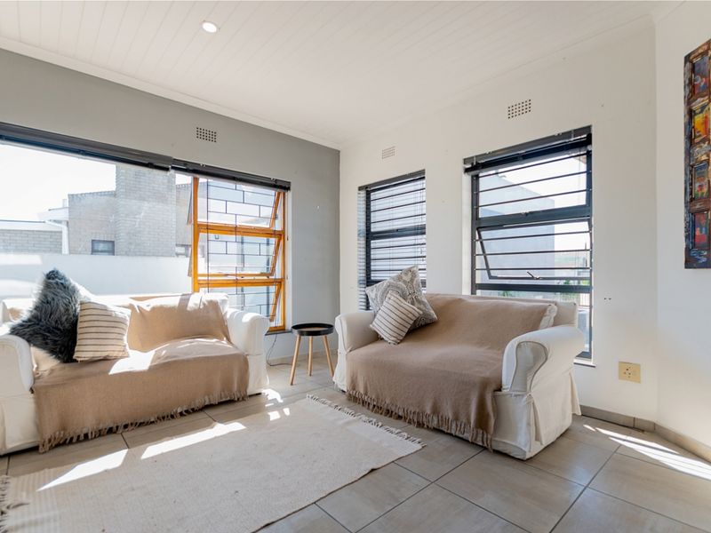 Bright living room featuring tiled flooring, large aluminium windows with security bars, and a clean, neutral aesthetic with recessed ceiling lighting.