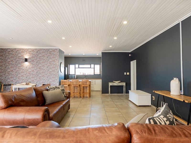 Spacious open-plan living area featuring tiled floors, a brick feature wall, and a modern kitchen with a central island and recessed lighting.