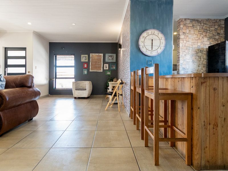 Spacious open-plan living area featuring tiled floors, a timber breakfast bar, and a striking stone feature wall with recessed lighting.