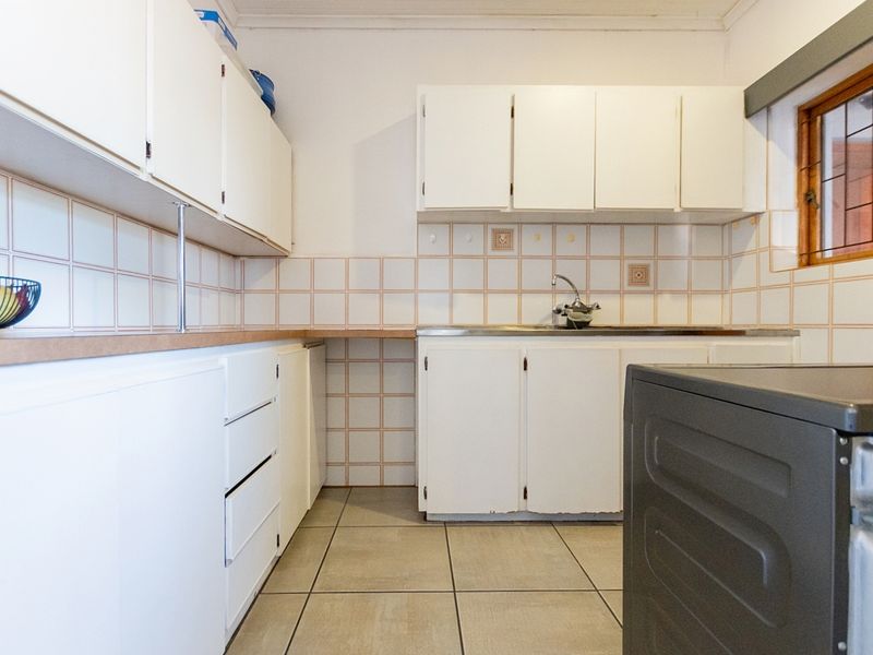 A functional kitchen featuring white built-in cabinetry, tiled backsplash, and tiled flooring, offering a practical layout with potential for modern updates.