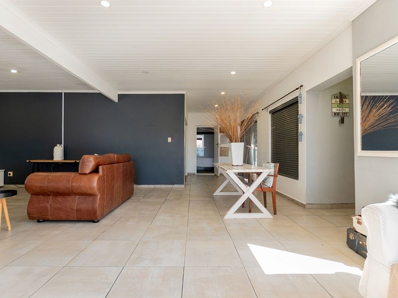 Spacious open-plan living area featuring neutral tiled flooring, a tongue and groove ceiling with recessed lighting, and a contemporary dark feature wall.