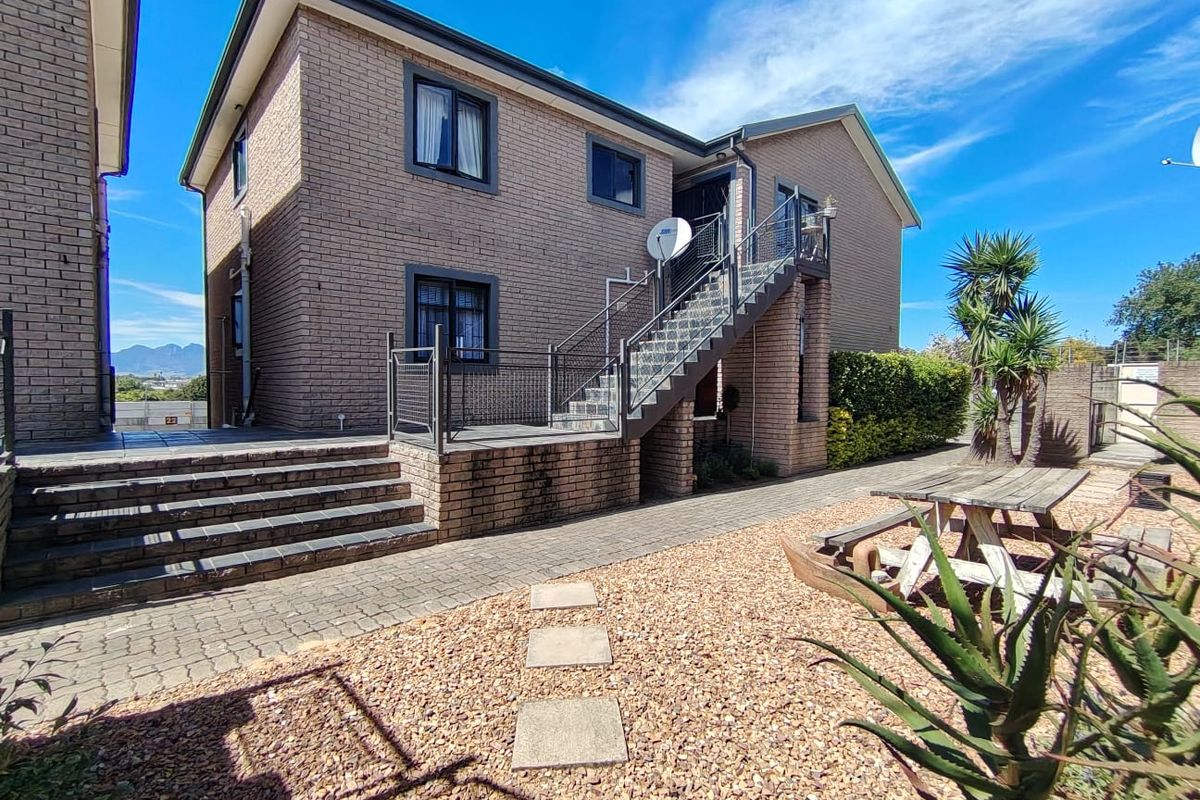Rear exterior view of a brick apartment building featuring an external staircase, paved patio area, and low-maintenance gravel garden.
