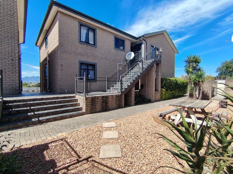 Rear exterior view of a brick apartment building featuring an external staircase, paved patio area, and low-maintenance gravel garden.