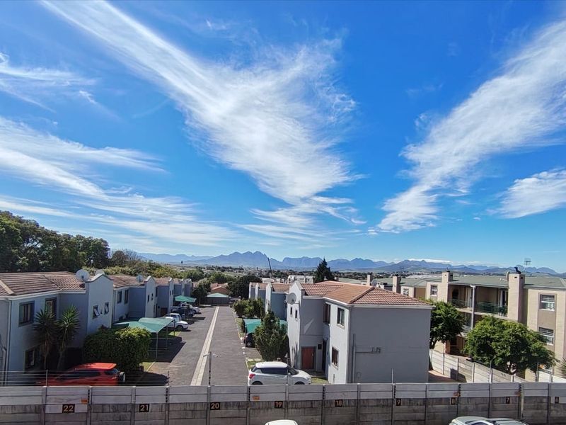 Elevated view overlooking the apartment complex grounds, paved driveway, and surrounding residential area with mountain views in the distance.