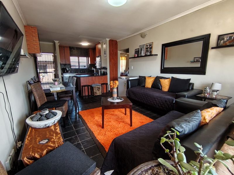 An open-plan living and kitchen area featuring dark tiled flooring, wooden cabinetry, and a breakfast counter, offering a functional layout for daily living.