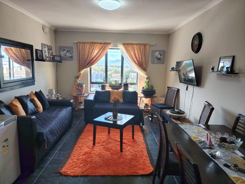 An open-plan living and dining area featuring tiled flooring, a large window with natural light, and neutral wall finishes.