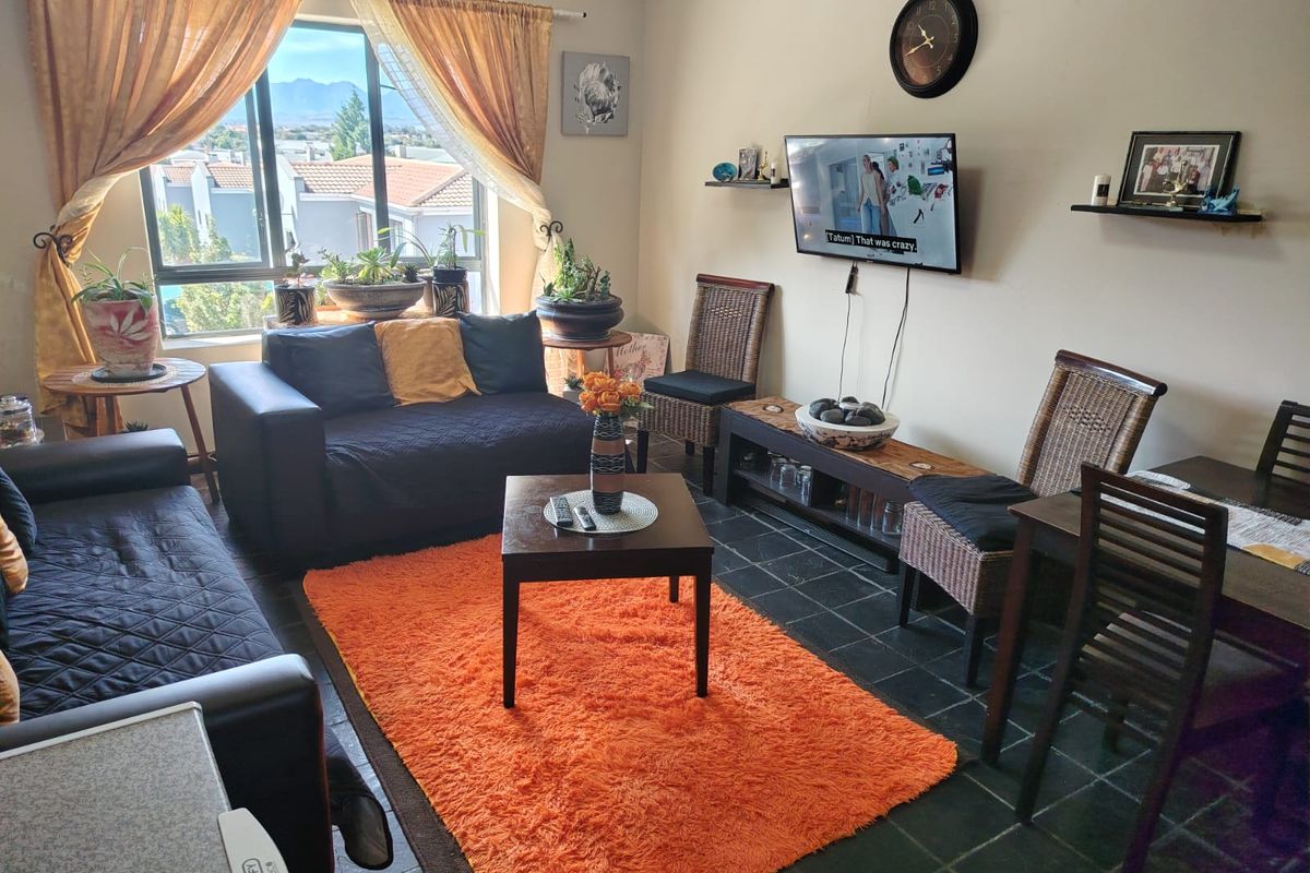 A comfortable living room featuring dark tiled flooring, a large window with natural light, and wall-mounted television connectivity.